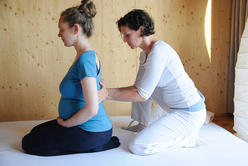 Shiatsu Behandlung bei einer sitzenden schwangeren Frau am Rücken